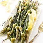 Roasted garlic spears on a serving platter with lemon wedges.