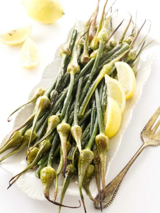 Roasted garlic spears on a serving platter with lemon wedges.