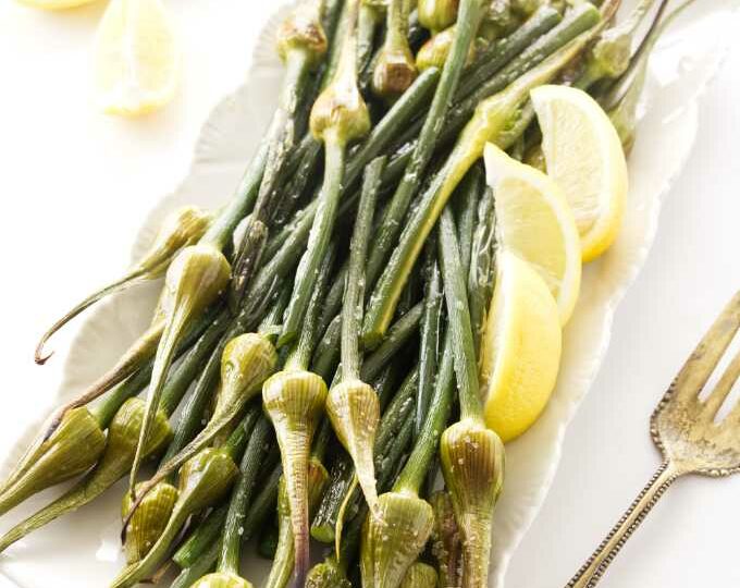 Roasted garlic spears on a serving platter with lemon wedges.