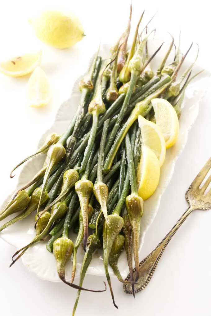 Roasted garlic spears on a serving platter with lemon wedges.