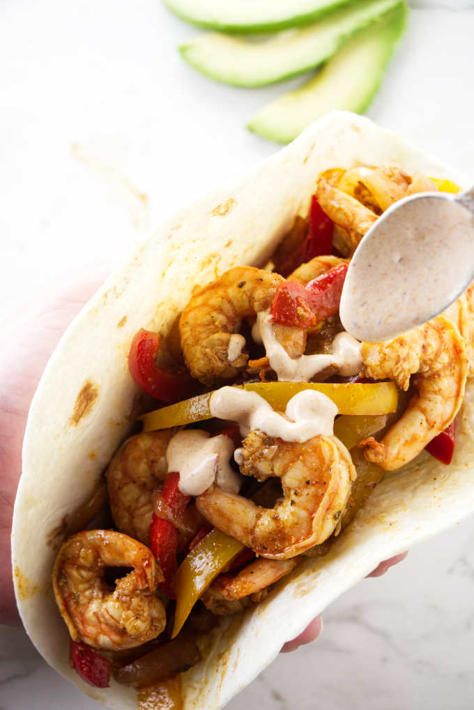 Shrimp fajita with a chipotle dressing being drizzled on top.