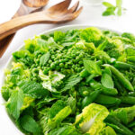 Overhead view of sugar snap pea salad, wooden serving utensils, buttermilk ranch dressing in background