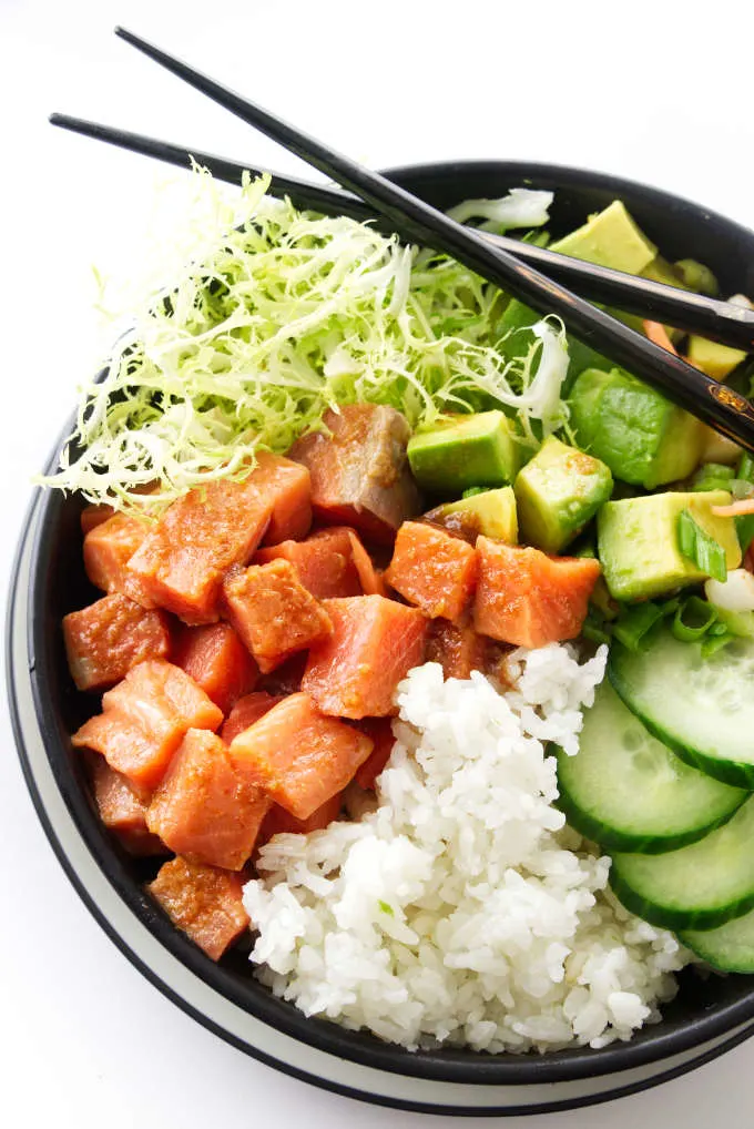 Spicy sushi bowl with salmon, avocado, cucumber, rice, green and chopsticks.