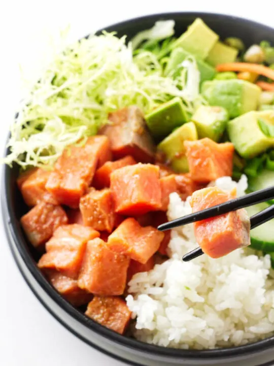 A bowl of spicy sushi, chopsticks lifting a salmon bite