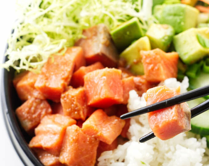 A bowl of spicy sushi, chopsticks lifting a salmon bite