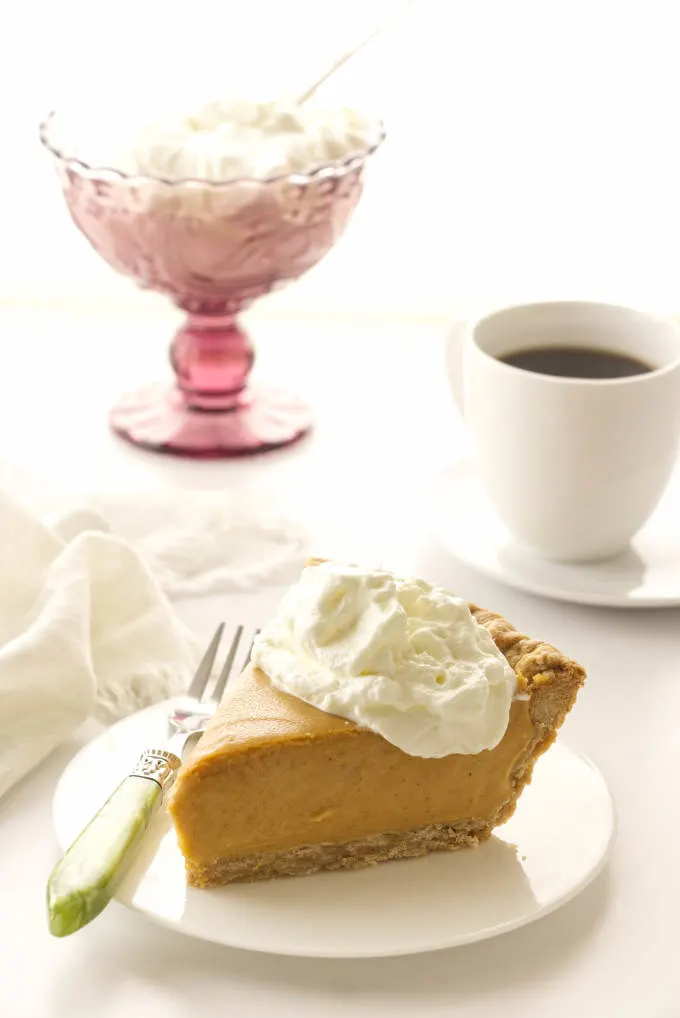 a slice of butterscotch cinnamon pie, cup of coffee and a dish of whip cream