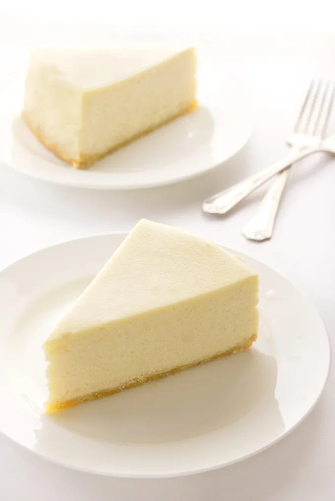 Two slices of cheesecake on plates, forks in the background
