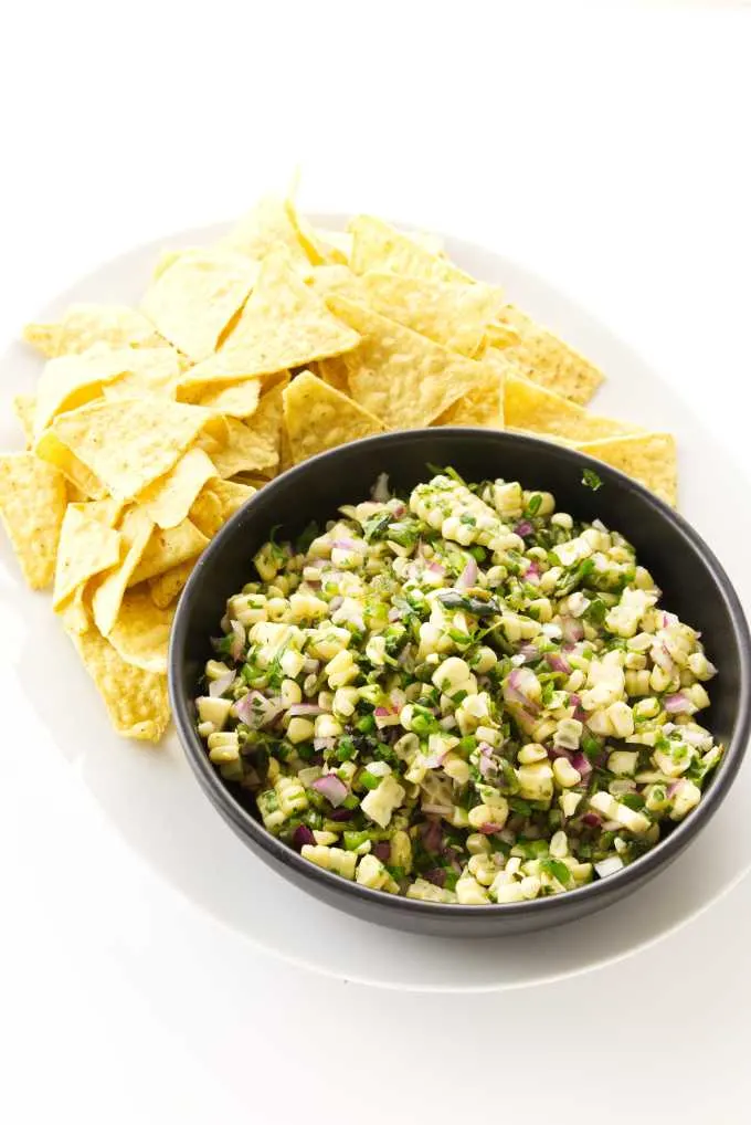 Bowl of chipotle corn salsa on a platter with corn tortilla chips