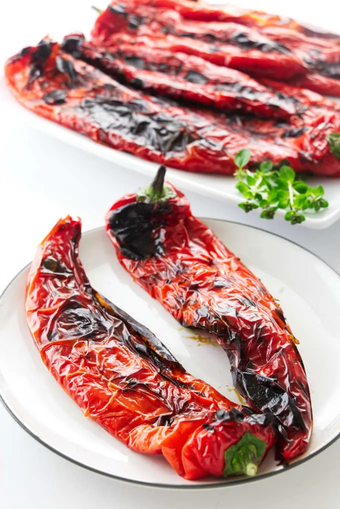 Two grilled sweet peppers on a plate with a serving platter in the background.