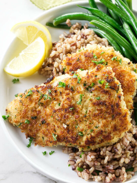 Two Panko crusted rockfish fillets on a dinner plate with rice and green beans.