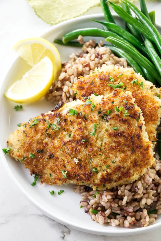 Two Panko crusted rockfish fillets on a dinner plate with rice and green beans.