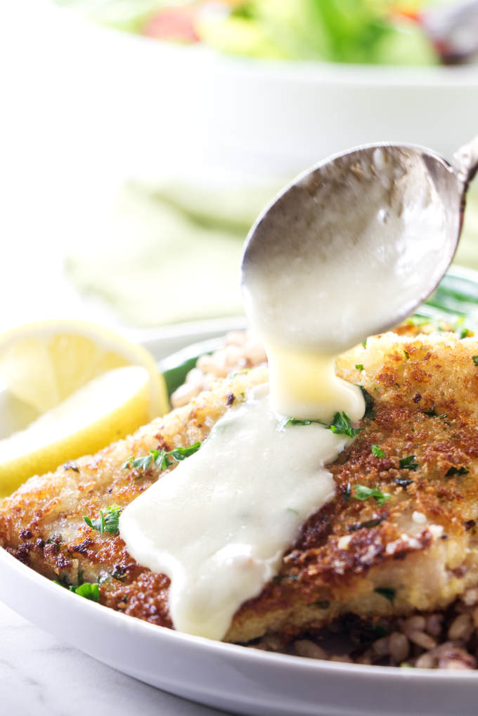 A spoon drizzling lemon sauce over a rockfish fillet.