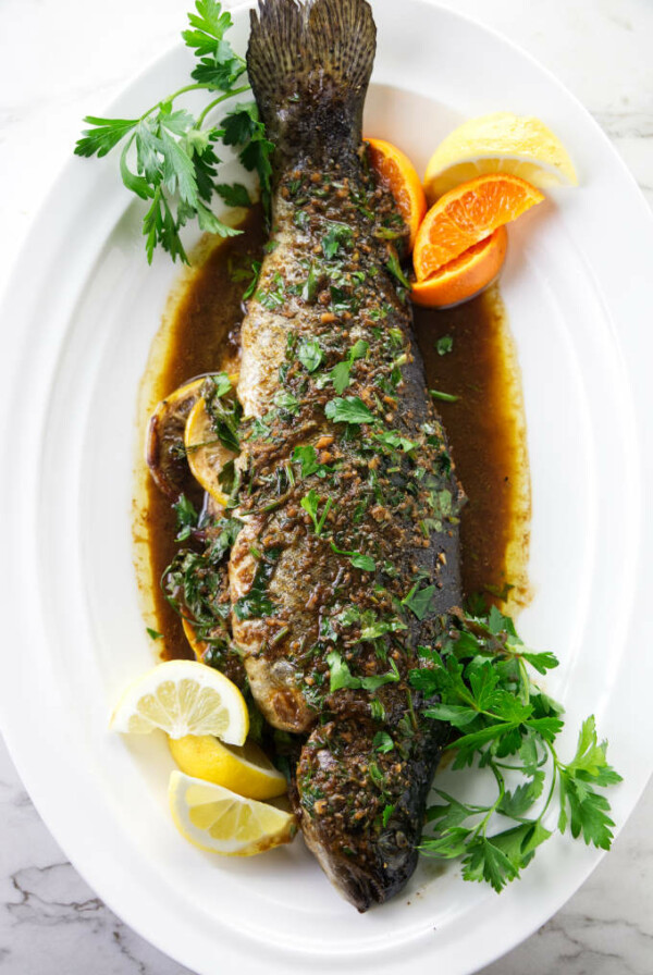 A whole baked rainbow trout on a serving platter.