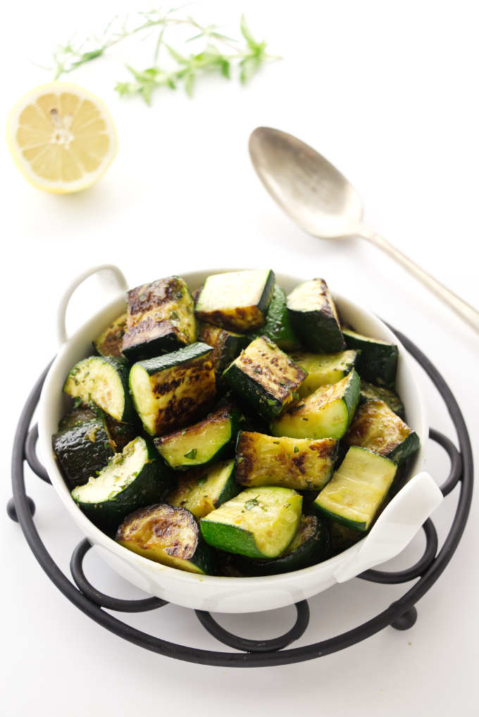 A serving dish of sautéed zucchini next to a lemon.