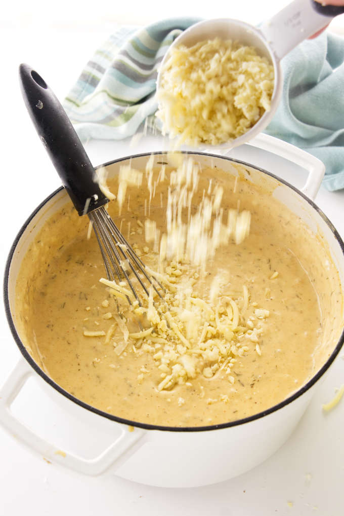 Adding noodles to cheese sauce in a large pot.