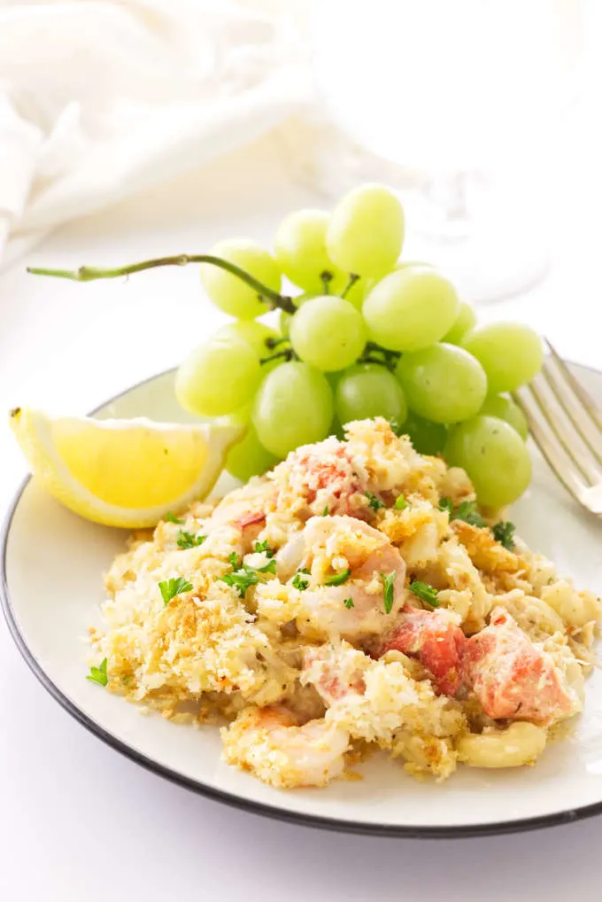 A plate with a serving of seafood mac and cheese and some grapes.