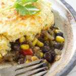 A serving of cornbread topped casserole on a plate with a fork.