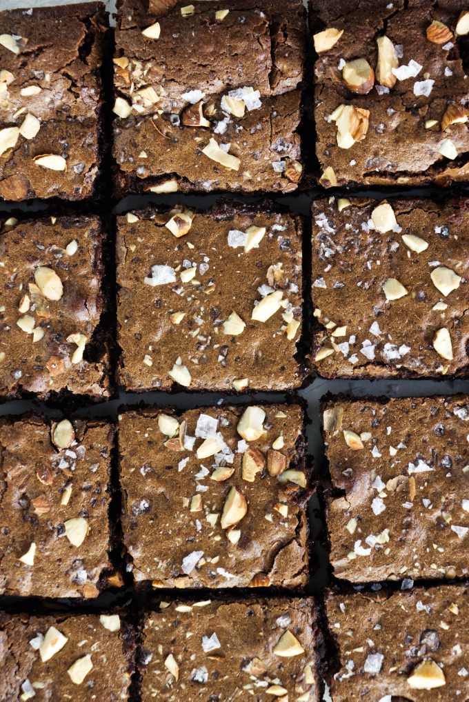 Twelve squares of brownies with almonds and salt flakes on top.