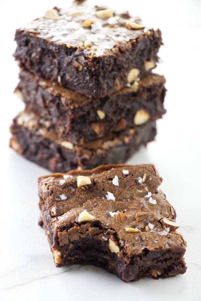 A partially eaten brownie in front of a stack of brownies with almonds.