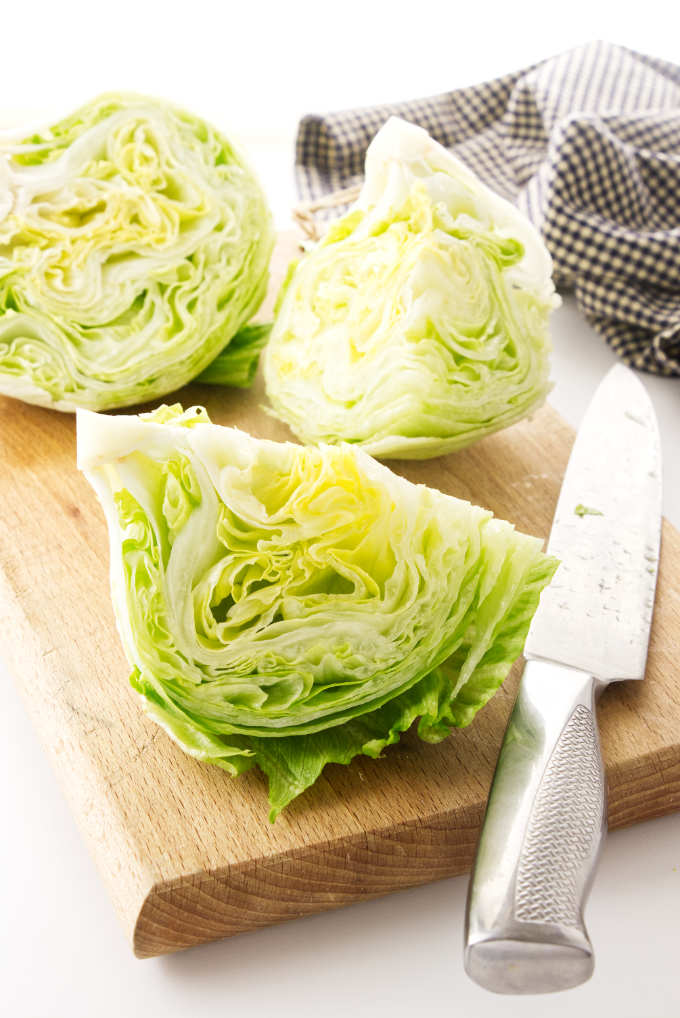 Iceberg lettuce on a cutting board with a knife.