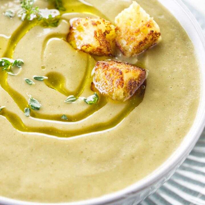 A bowl of zucchini garlic soup with croutons and olive oil on top.