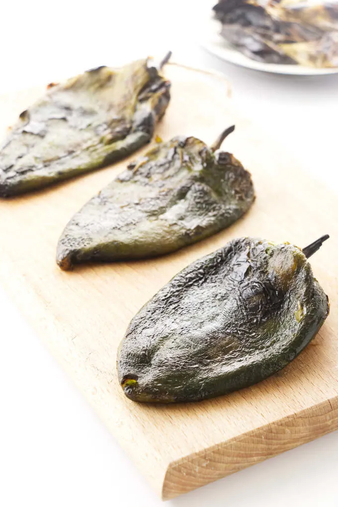 Roasted poblano peppers on a cutting board.