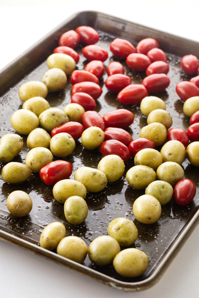 A baking tray with baby potatoes and grape tomatoes.