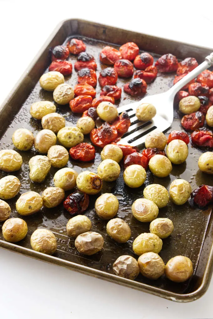 Roasted potatoes and tomatoes on a baking sheet.