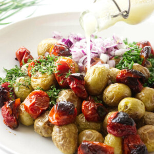 Salad dressing being poured over a roasted potato salad.