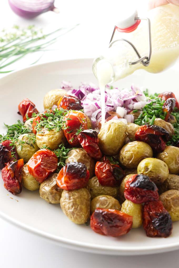 Salad dressing being poured over a roasted potato salad.