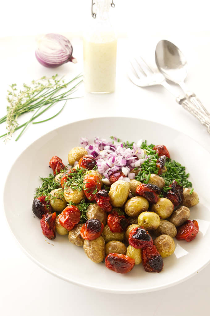 Roasted potatoes and salad ingredients getting tossed in a bowl.