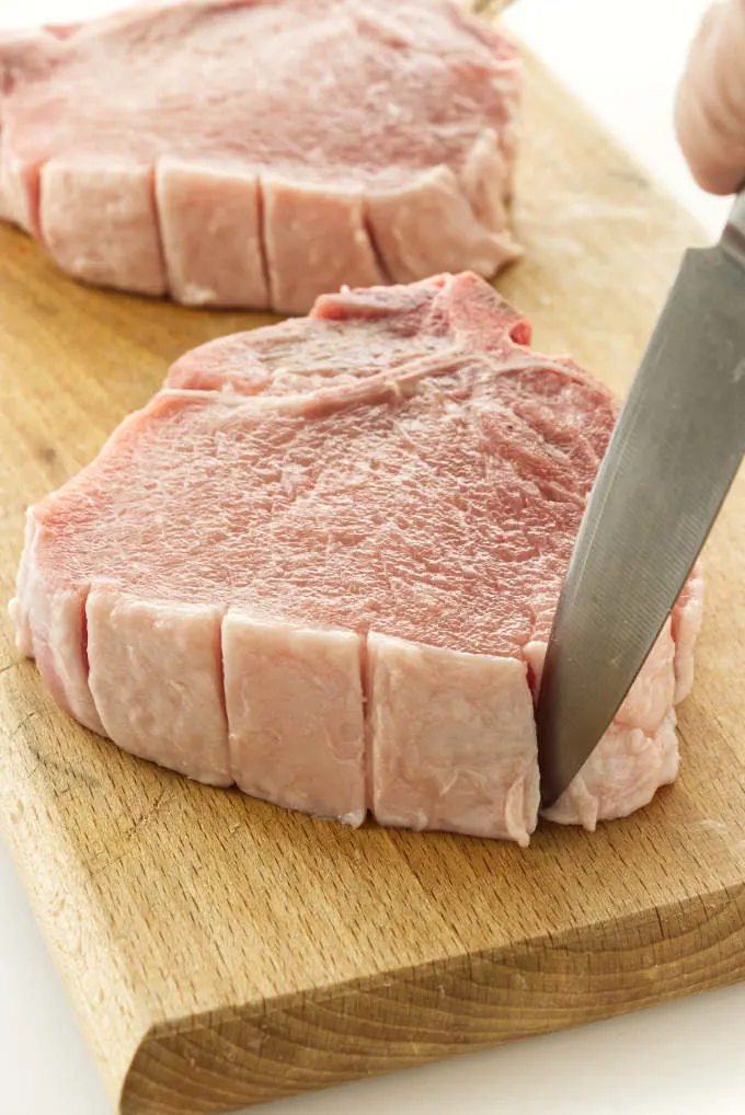 Showing how to slice the fat layer on the edge of pork chops.