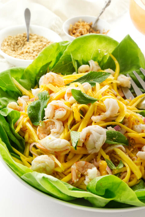 A serving dish of Vietnamese green mango salad with chopped peanuts and crispy shallots in the background.