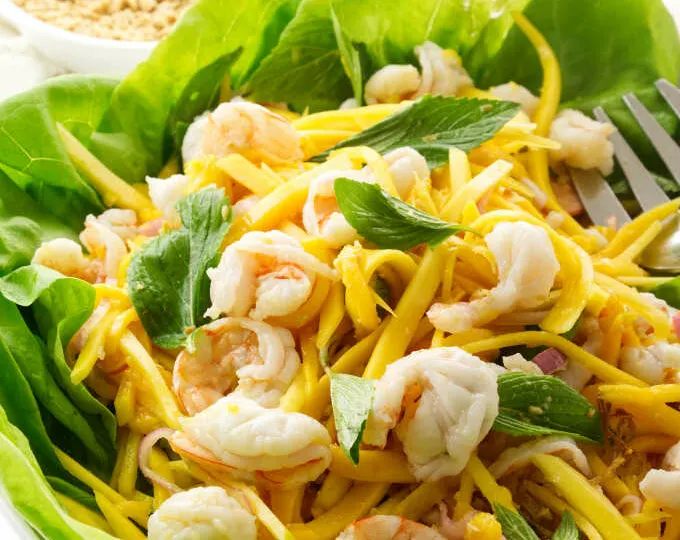 A serving dish of Vietnamese green mango salad with chopped peanuts and crispy shallots in the background.