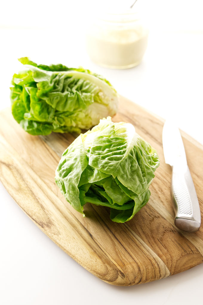 Two heads of Little Gem lettuce on cutting board with knkfe. Caesar salad dressing in background.