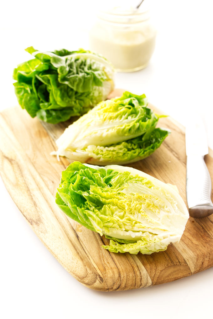 A head of Little Gem lettuce, cut in half on a cutting board with un-cut head