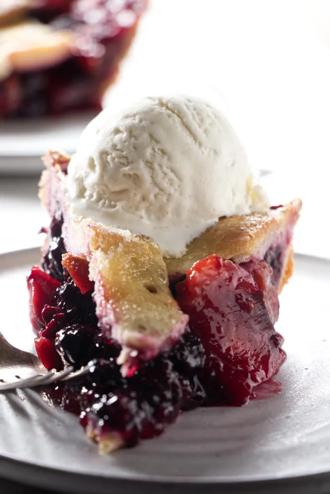 A slice of blackberry peach pie with vanilla ice cream on top.