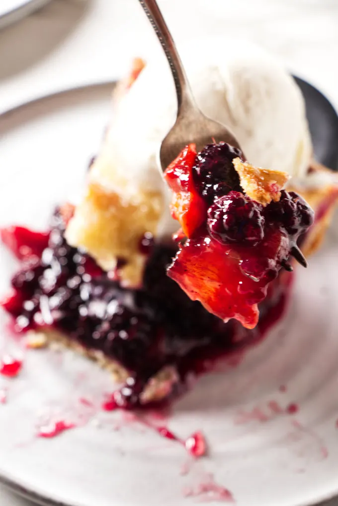 A fork holding a bite of a blackberry peach pie.