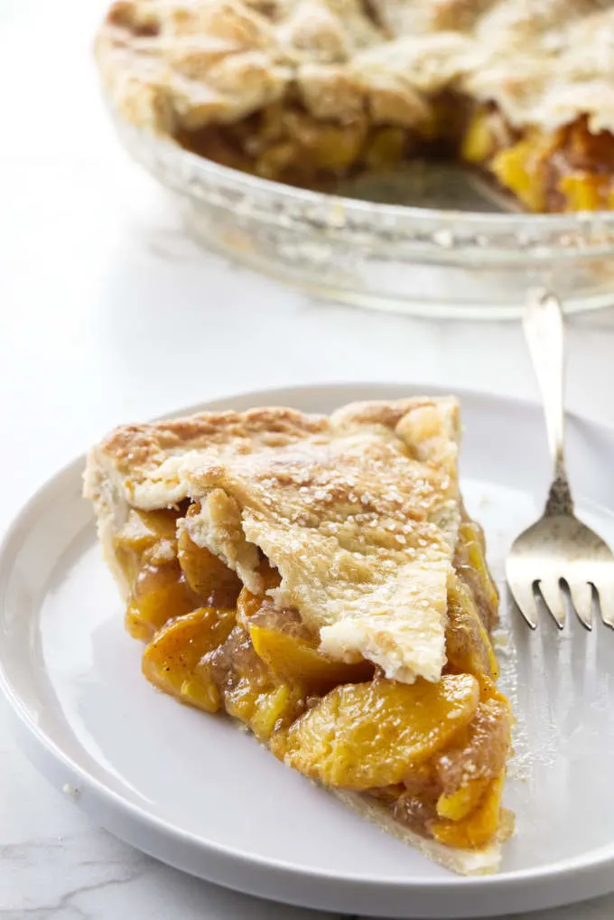 A slice of brown butter bourbon peach pie with a pie dish in the background.