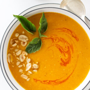 Overhead view of Thai butternut ginger soup garnished with chopped peanuts, chili oil and Thai basil leaves.