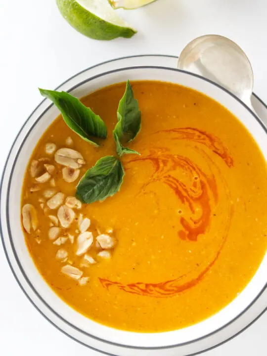 Overhead view of Thai butternut ginger soup garnished with chopped peanuts, chili oil and Thai basil leaves.