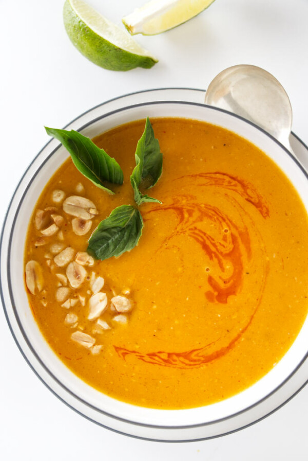 Overhead view of Thai butternut ginger soup garnished with chopped peanuts, chili oil and Thai basil leaves.