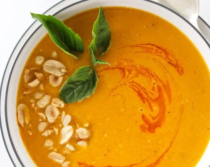 Overhead view of Thai butternut ginger soup garnished with chopped peanuts, chili oil and Thai basil leaves.