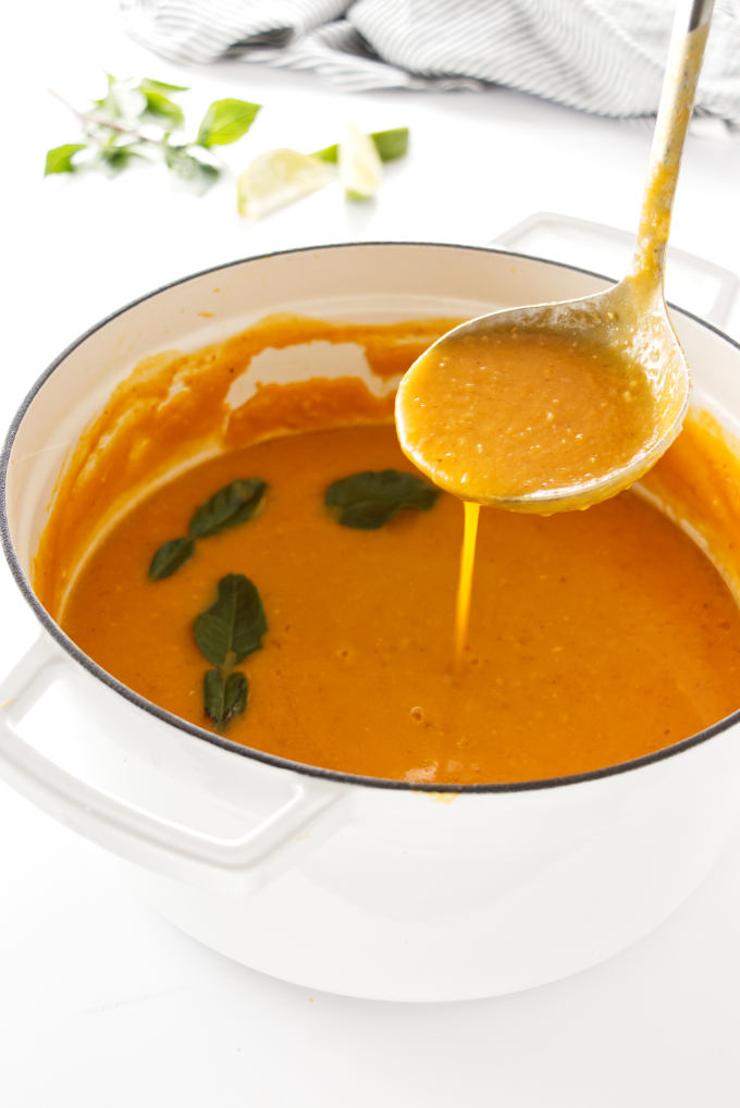 Soup pot of butternut squash soup with kaffir lime leaves and a ladle of soup