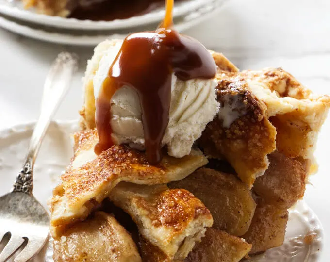 Pouring caramel sauce over an apple pie with vanilla ice cream.