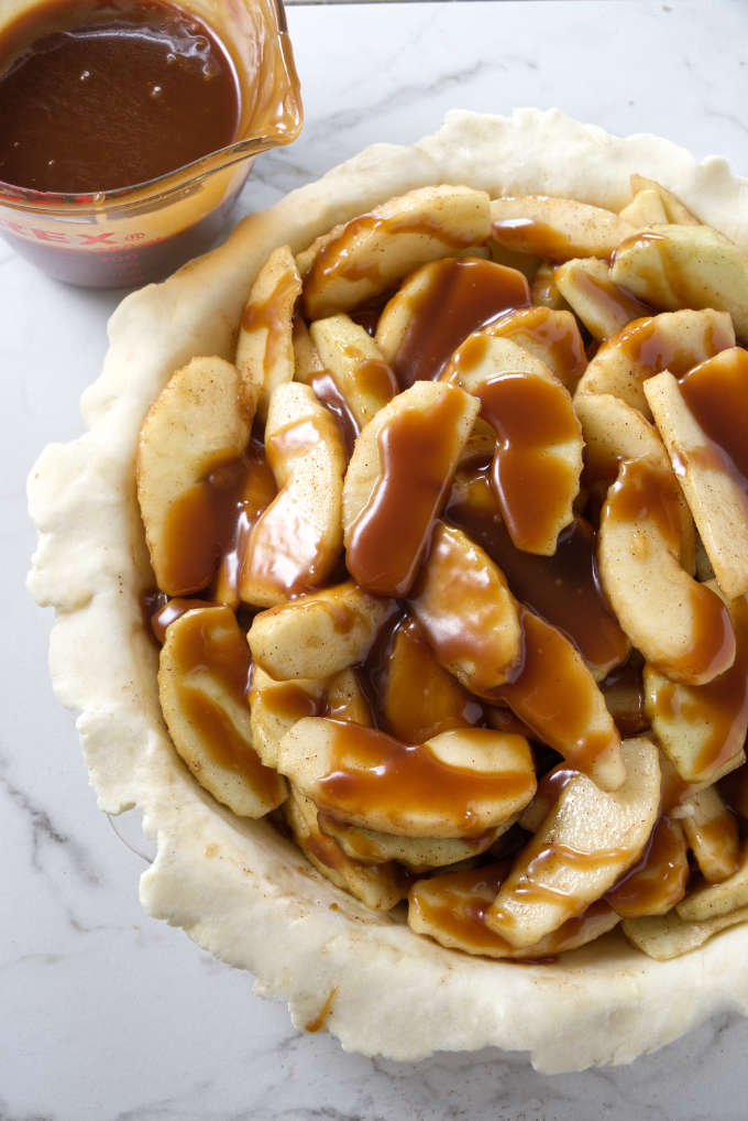 Apple pie filling in a pie shell with caramel sauce on top of the apples.