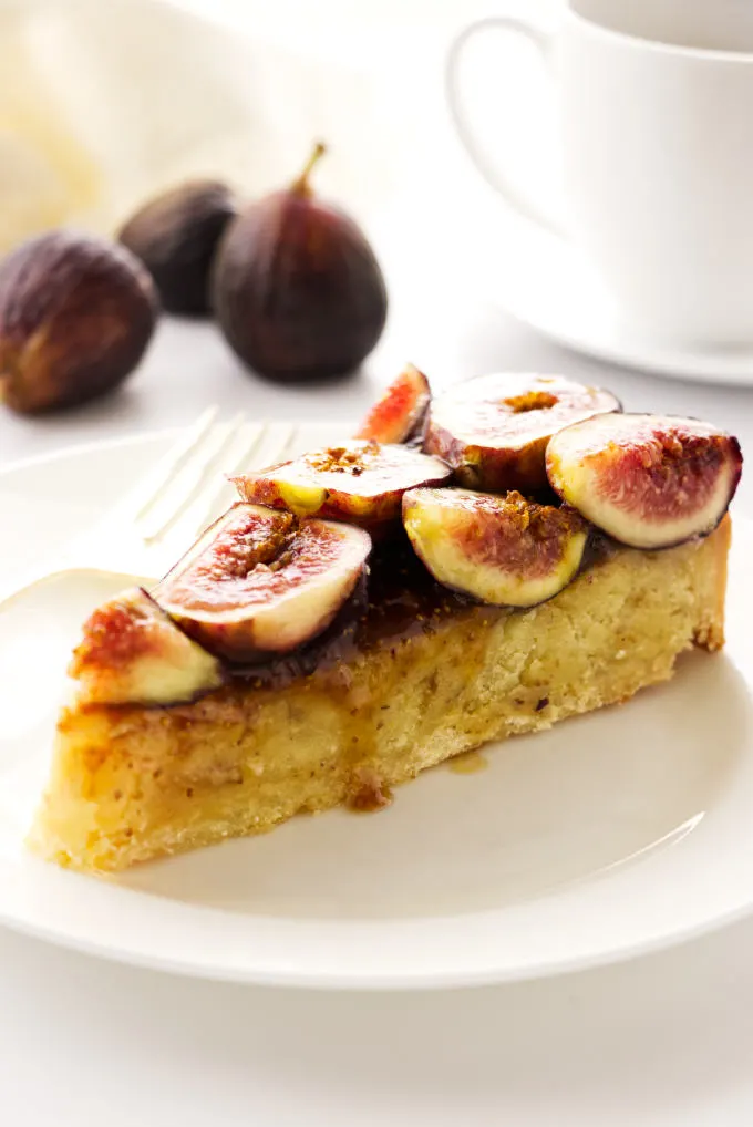 a slice of fig frangipane tart, cup of coffee and figs in background