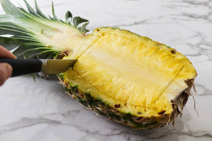 Carving around the perimeter of the inside of half of a pineapple.
