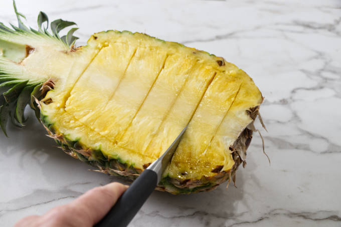 Slicing horizontal lines into a pineapple half.