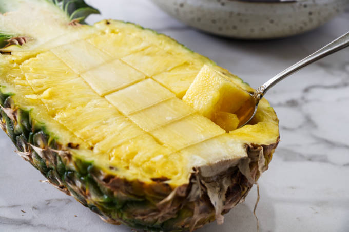 Scooping out a chunks of fruit in half of a pineapple.
